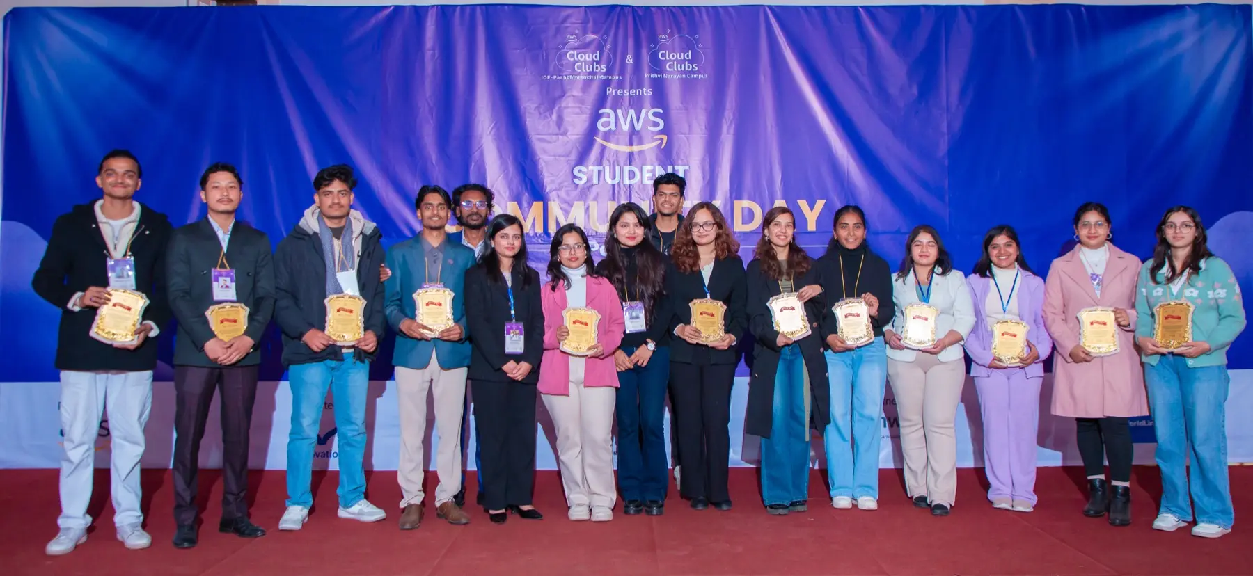 Line of award recipients holding golden plaques on a red-carpeted stage in front of the AWS Student Community Day backdrop