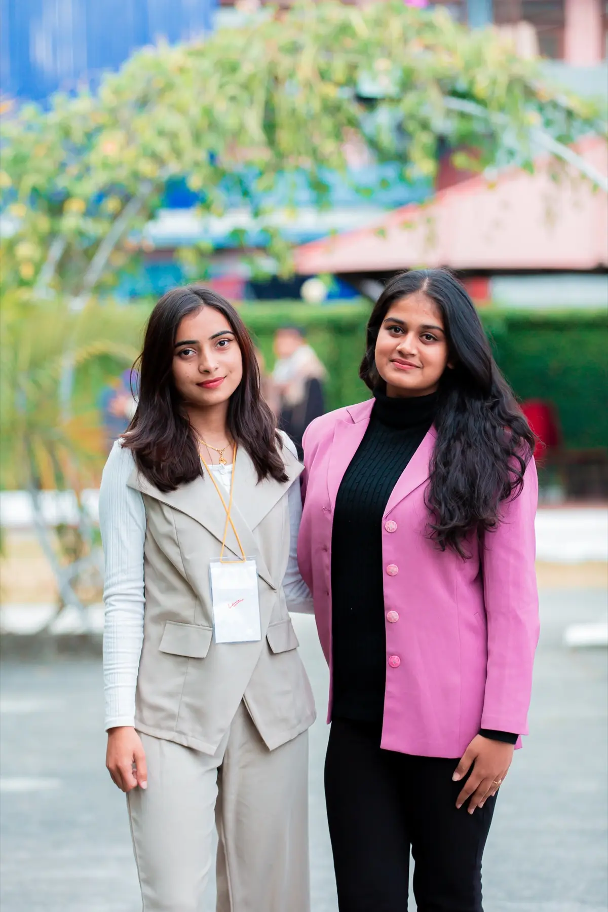 Two women, one in a beige waistcoat and one in a pink blazer, posing together outdoors at the venue